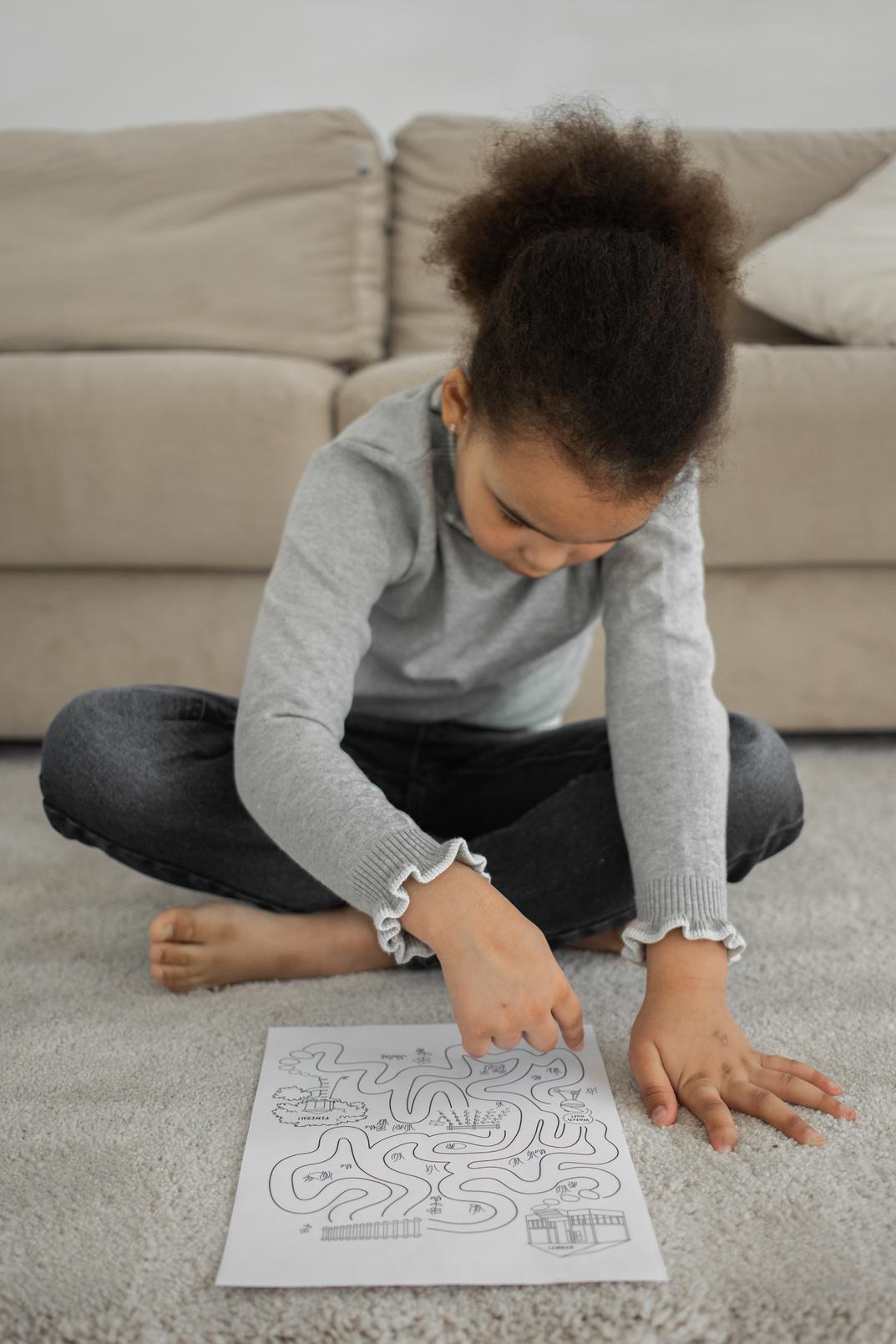Focused ethnic kid solving printed labyrinth on paper